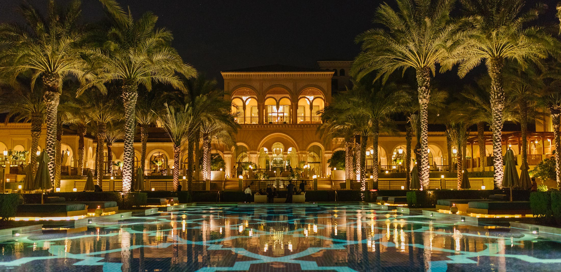 Palm-lined courtyard and reflecting pool of a candlelit palace venue at night